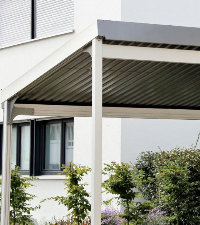 Carport mit Metalldach und weißer Wand, bietet Schutz für Fahrzeuge und ergänzt die Umgebung stilvoll.